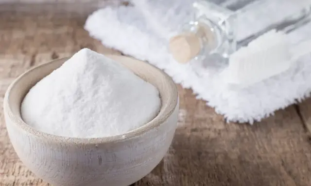Soda oczyszczona w miseczce, obok ręcznik, buteleczka i szczoteczka. Czy soda oczyszczona odbarwia ubrania?