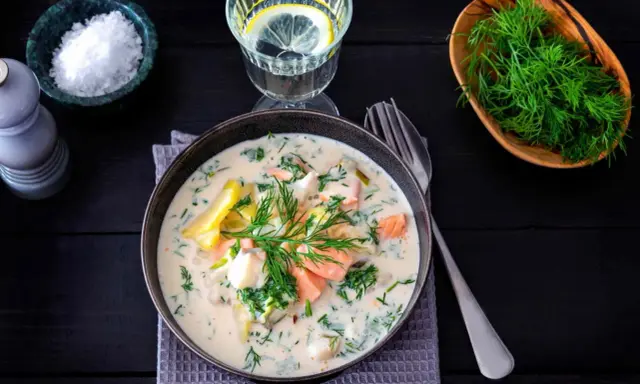 Krämig fisksoppa med lax och dill, en av många lyxiga fiskrecept. Serveras med citronvatten och havssalt.
