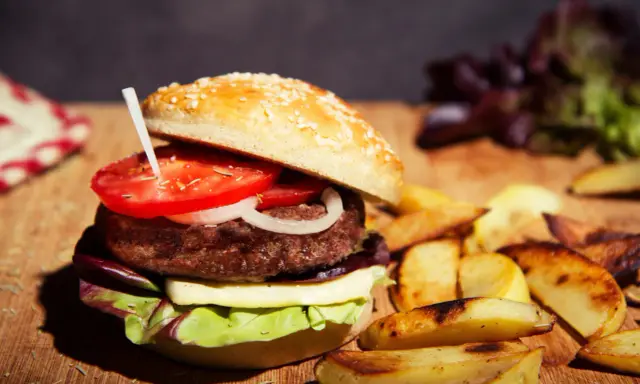 Burger maison avec pain aux graines, tomate, oignon, fromage et salade. Accompagné de frites. Une recette pain burger sans gluten à essayer !