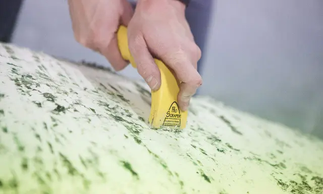 Mains utilisant un grattoir électrique antifouling pour enlever des résidus verts sur une surface.