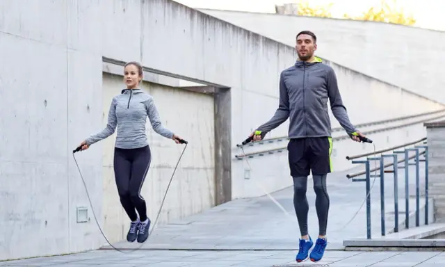 Ein Paar macht ein intensives **Springseil Workout** im Freien vor einer Betonwand.