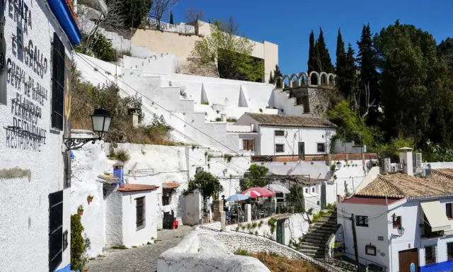 Weiße Häuser und Terrassen im Sacromonte, Granada, mit Kopfsteinpflaster und blühenden Pflanzen.