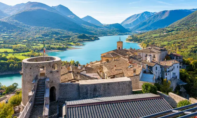 Borgo medievale con torre e lago turchese, incastonato tra i monti dell'Abruzzo.