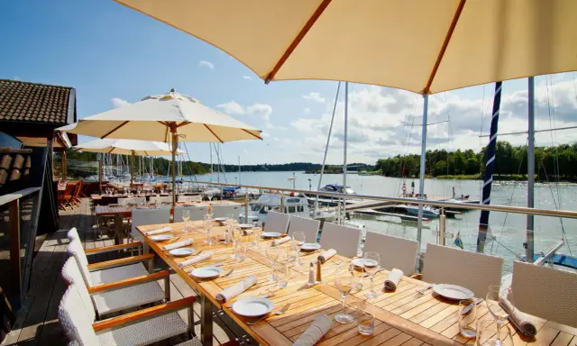 Väl dukade bord på en restaurang vid havet med segelbåtar i bakgrunden.