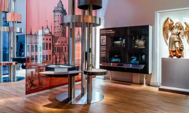 Utställning på ekonomiska museet med en stor illustration av en stad, en skulptur av en ängel och interaktiva displayer.