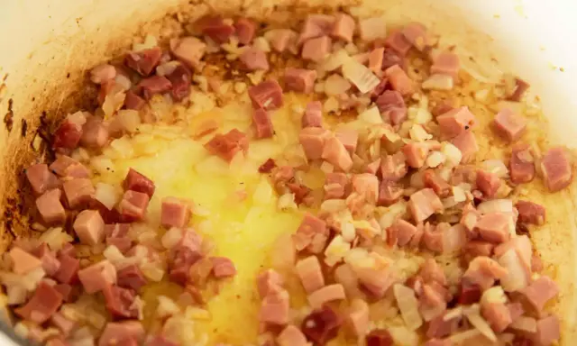 Guisantes con jamón y cebolla dorándose en una sartén con aceite. Un plato tradicional español.