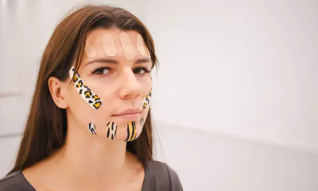 Kobieta z kolorowymi plastrami na twarzy, stosuje taping twarzy dla poprawy wyglądu.