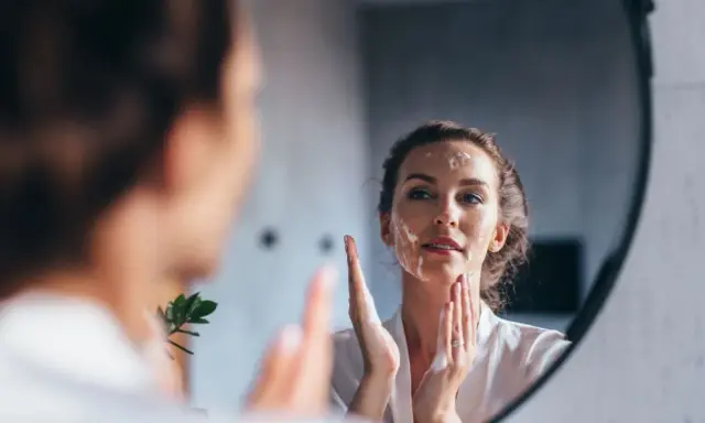 Une femme se regarde dans un miroir, appliquant de la mousse sur son visage pour un double nettoyage.