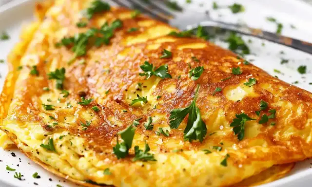 En gyllene omelett, perfekt för ett snabbt omelett recept, toppad med färsk persilja och en nypa salt.