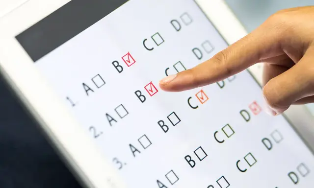 Palec wskazuje odpowiedź B na ekranie tabletu, gdzie trwa test baltimorski. Zaznaczone są już odpowiedzi B i C.