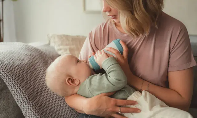 Mutter füttert Baby mit Flasche. Das Baby trinkt langsam, um die Verdauung zu unterstützen.