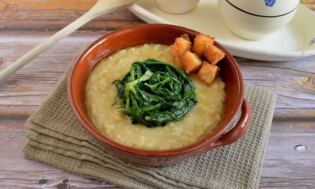 Piatto di fave e cicoria, una crema gialla con verdura verde al centro e crostini dorati.