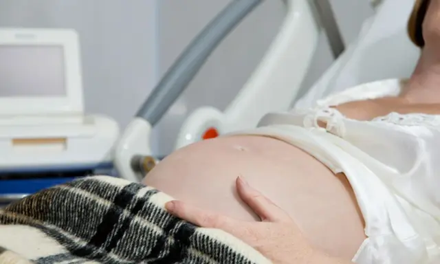Kobieta w szpitalnym łóżku, z ręką na brzuchu, czeka na poród. Obok monitor KTG, który pomaga ocenić, jak przyspieszyć rozwarcie.