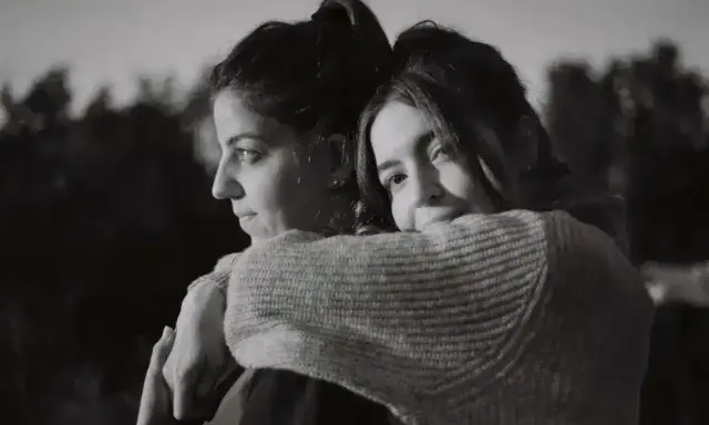 Dos mujeres se abrazan, una mirando al horizonte con **miedo al abandono**, la otra la abraza con ternura.