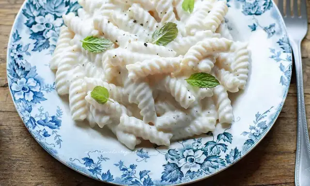 Fusilli cremosi conditi con una salsa vellutata alla ricotta, guarniti con foglie di menta fresca su un piatto decorato.