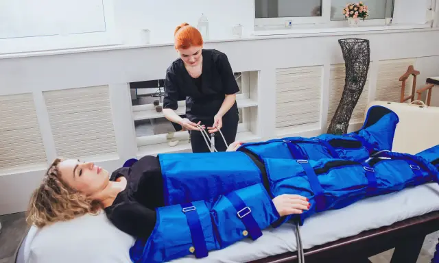 Kobieta w salonie piękności poddawana zabiegowi, który wyjaśnia, co to jest drenaż limfatyczny. Terapeuta przygotowuje urządzenie do masażu uciskowego.
