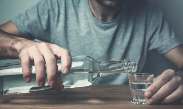 Mężczyzna nalewa alkohol do kieliszka. Nadmierne spożycie alkoholu negatywnie wpływa na żyły, prowadząc do ich uszkodzenia.