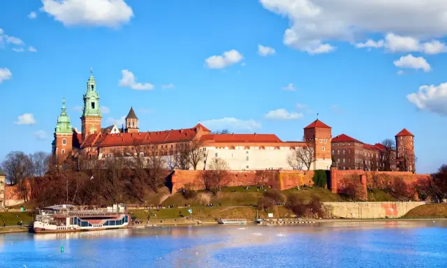 Zamek Królewski na Wawelu, z zielonymi wieżami i czerwonymi dachami, góruje nad Wisłą. Ciekawostki o jego historii czekają na odkrycie.