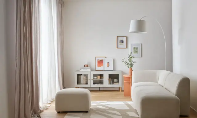 Jasny, długi wąski pokój w bloku z wygodną sofą, pufą i nowoczesną szafką. Zasłony wpuszczają dużo światła.