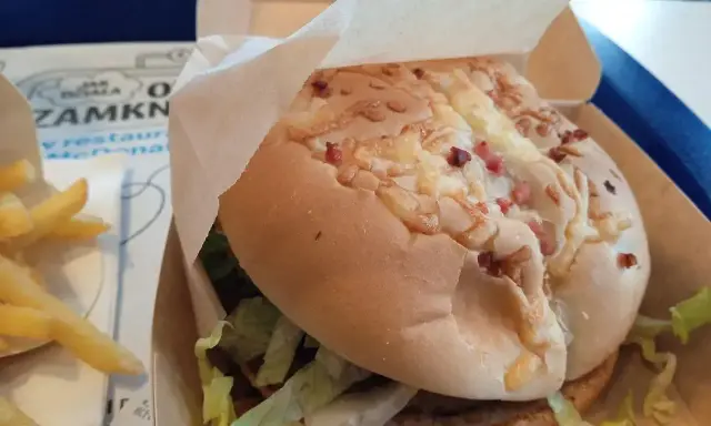 Pyszny burger drwala z chrupiącym bekonem i serem, w papierowym opakowaniu, obok porcji frytek.