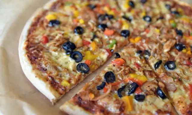 Pyszna pizza sycylijska z oliwkami, papryką i serem, pokrojona na kawałki.