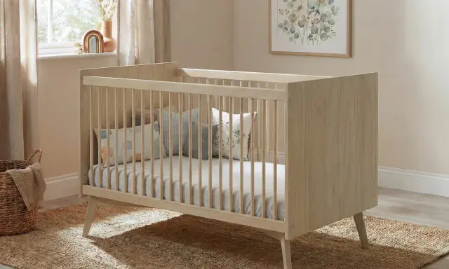 Cuna de madera clara con barrotes, colchón y cojines decorativos. Las medidas cuna son ideales para un cuarto infantil acogedor.