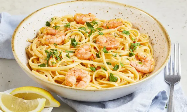 Eine Schüssel mit Spaghetti mit Garnelen, garniert mit Petersilie und Chiliflocken. Dazu Zitronenspalten und eine Gabel.