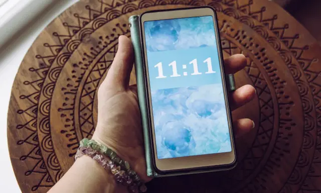 Dłoń trzyma telefon z wyświetloną godziną 11:11, co dla wielu ma szczególne znaczenie.