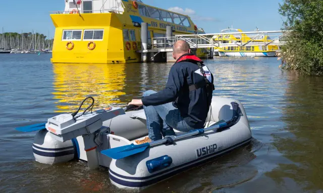 Un homme pilote un bateau gonflable propulsé par la puissance d'un moteur électrique, naviguant près d'un grand bateau jaune.