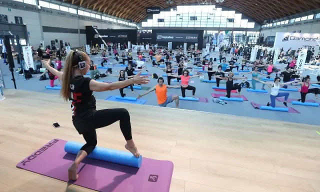 Allenamento di gruppo alla fiera dello sport Rimini, con istruttrice e partecipanti su tappetini.