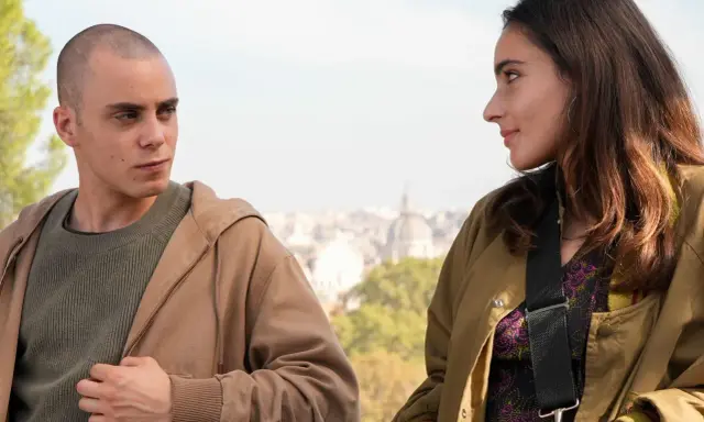Due giovani si guardano intensamente, come se fossero in una "casa degli sguardi". Lui, rasato, lei con lunghi capelli castani.