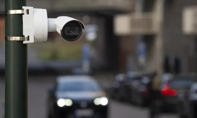 Cámara de seguridad blanca montada en poste, capturando el tráfico con su sensor global shutter.