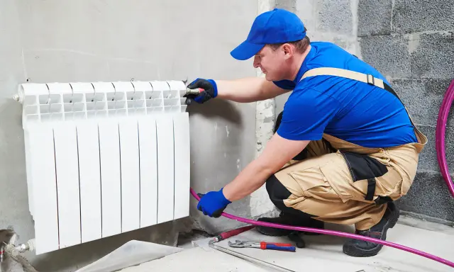 Un plombier effectue le branchement radiateur eau. Il installe un nouveau radiateur blanc sur un mur en béton.