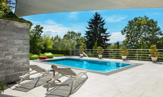 Moderne idee aiuole bordo piscina: piante in vaso e pouf colorati creano un'oasi rilassante.