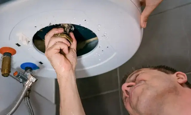 Main qui répare un chauffe-eau, une fuite d'eau s'échappe du cumulus qui fuit par le haut.