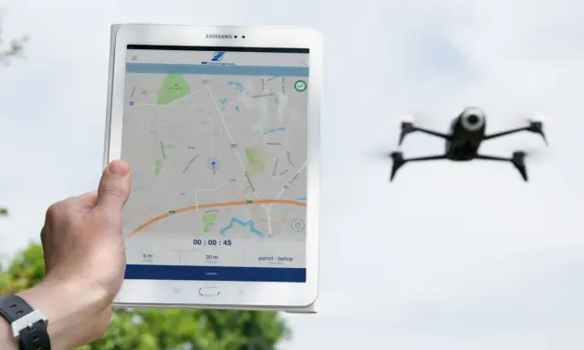 Tablet zeigt eine Karte und Drohnen-Apps. Eine Drohne fliegt im Hintergrund.