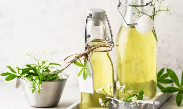 Zwei Flaschen mit selbstgemachtem Waldmeistersirup, dekoriert mit frischen Waldmeisterzweigen und kleinen weißen Blüten.