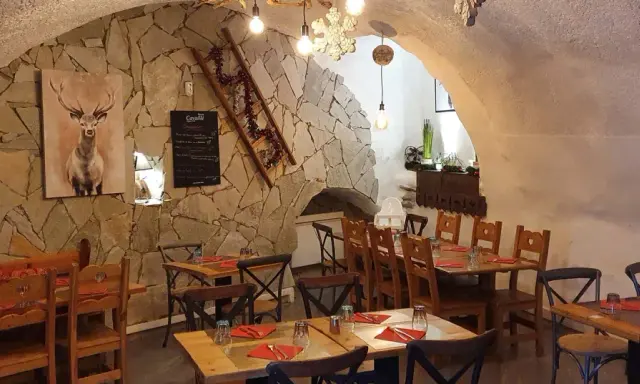 Ambiance chaleureuse dans un des restaurants de Briançon. Murs en pierre, tables en bois, tableau de menu et décoration hivernale.