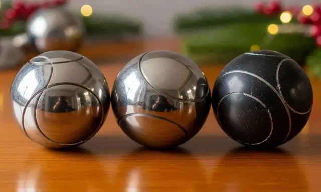 Trois boules de pétanque, deux argentées et une noire, sur une table en bois. Parfait pour un règlement pétanque simplifié.