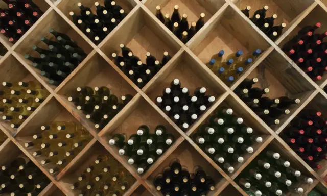 Holzregal mit vielen Flaschen Wein, ideal zum rotwein lagern. Verschiedene Sorten und Farben sind zu sehen.