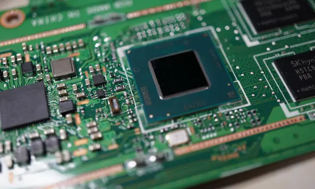 Zbliżenie na zieloną płytę główną z widocznymi częściami laptopa: procesorem, układami pamięci i innymi komponentami elektronicznymi.