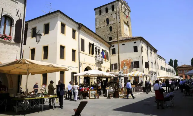 Mercato in piazza a Portobuffolè cosa vedere: bancarelle di antiquariato e la torre civica sullo sfondo.