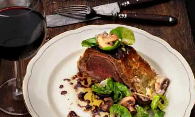 En saftig wellington biff serveras med svamp och grönsaker, ackompanjerad av ett glas rött vin.