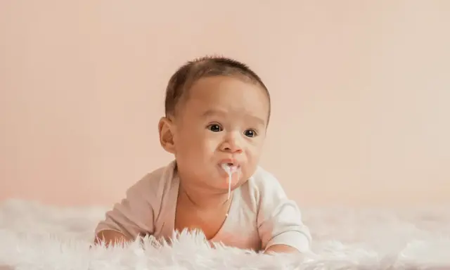 Söt bebis med mjölk runt munnen, ser ut som att bebis spyr mycket.