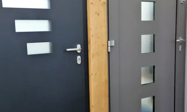 Dwie nowoczesne drzwi wejściowe, ciemnoszare i szare, z przeszkleniami. Ocieplenie drzwi wejściowych to klucz do komfortu.