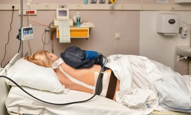 Pacjentka w łóżku szpitalnym z aparaturą medyczną. Widać cewnik z lekiem, co może być związane z pytaniem: epidural co to.