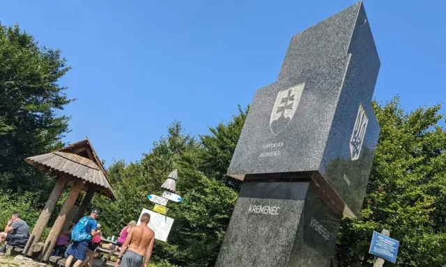 Trójstyk granic Bieszczady: monument z herbami Słowacji i Ukrainy, drewniana wiata i turyści.