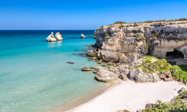 Scogliere calcaree e mare cristallino a Torre dell'Orso centro, con faraglioni che emergono dall'acqua turchese.