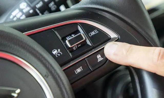 Palec naciska przycisk aktywujący tempomat. Widoczne przyciski: RES+, SET-, LIMIT, CANCEL.