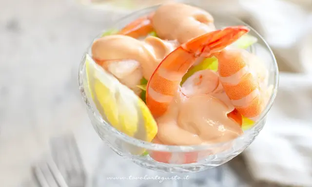 Un delizioso cocktail di gamberi servito in una coppa di cristallo, con una fetta di limone e una salsa rosa cremosa.